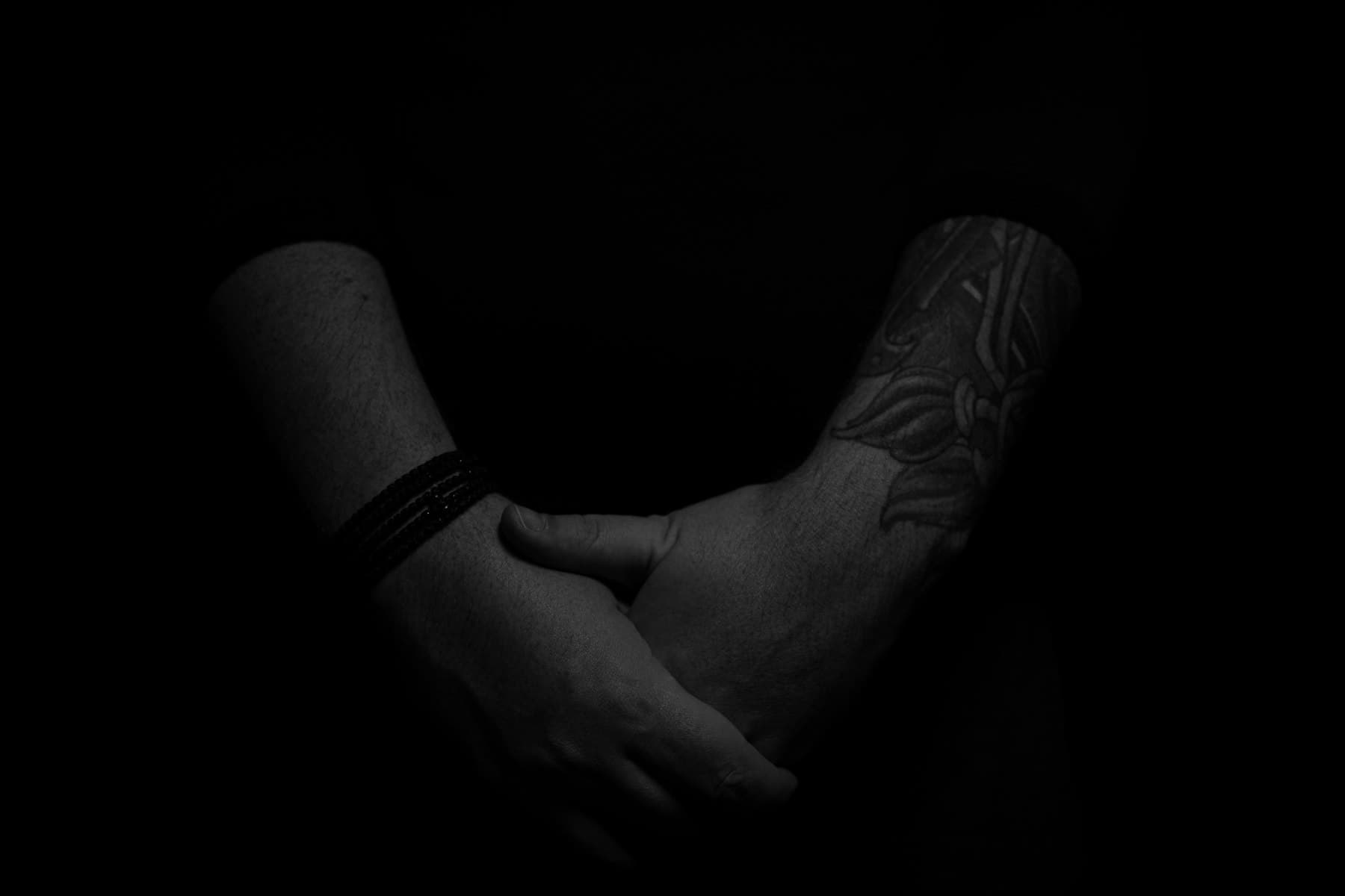 Tattooed hands folded in shadow