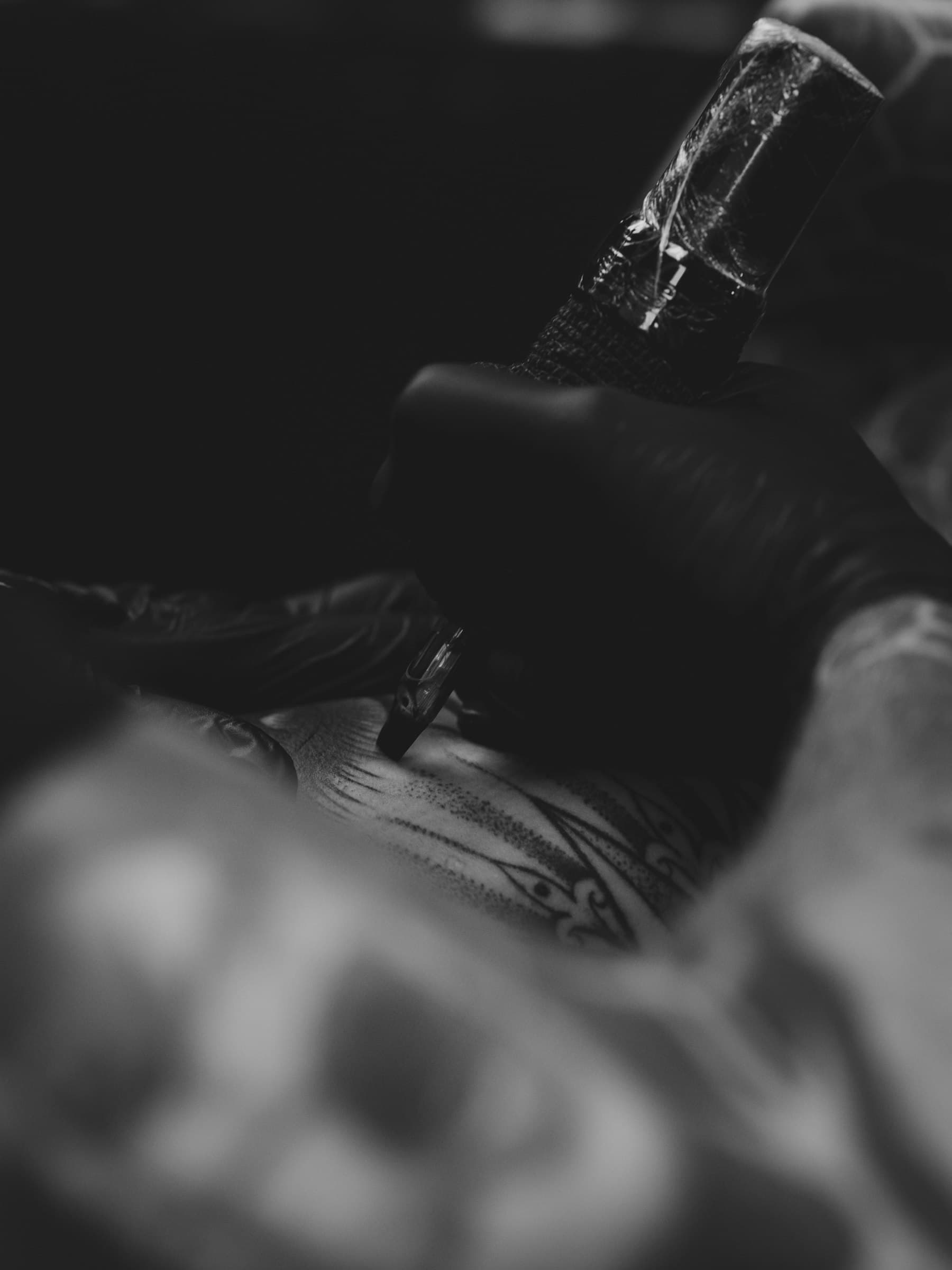A tattoo machine at work on an arm, seen in low light